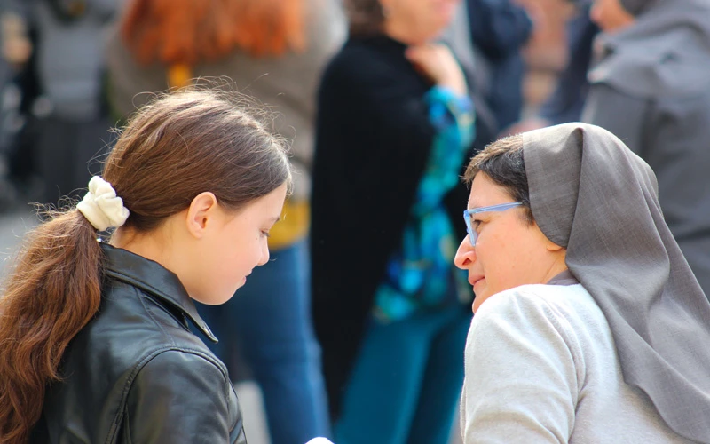 Suora salesiana e una giovane ragazza in primo piano mentre conversano all'aperto