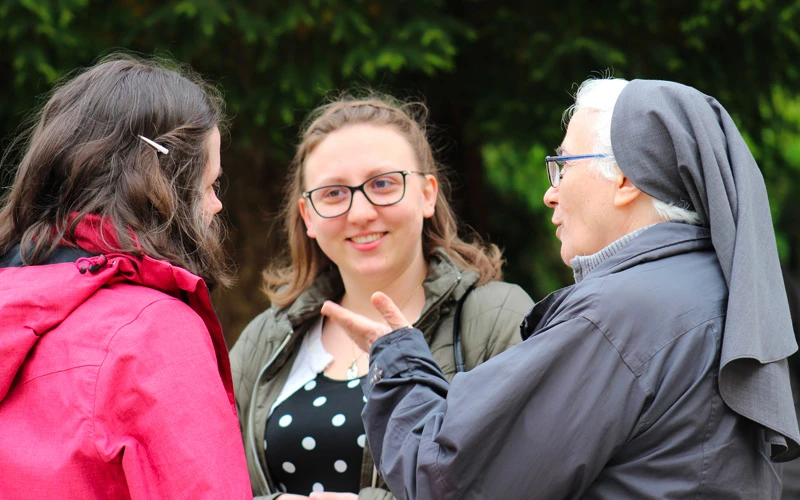 Suora anziana che parla e si confronta sorridendo con due giovani ragazze all'aperto