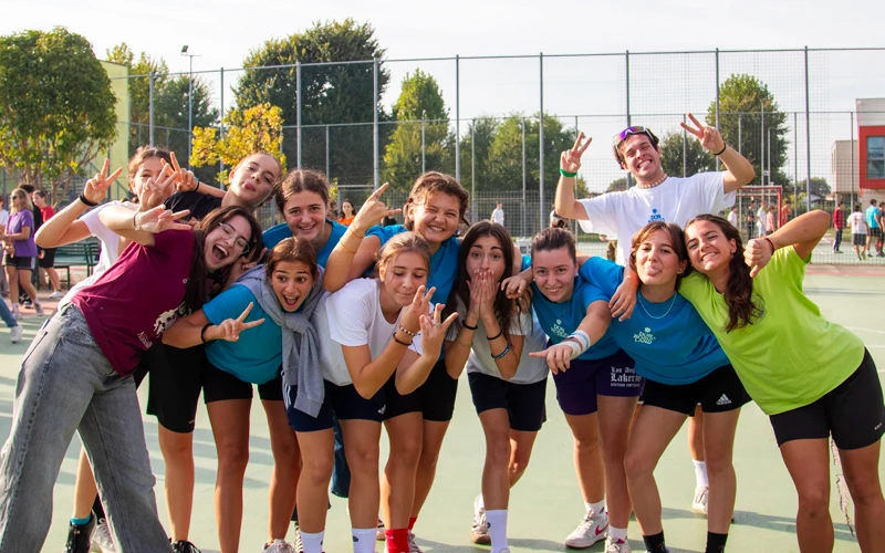 Gruppo di giovani animatori dell'oratorio che sorridono e fanno gesti festosi nel campo sportivo all'aperto